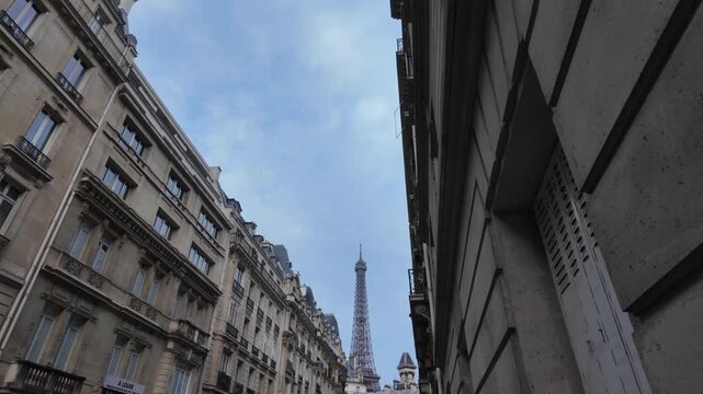 Eiffel tower rising between traditional parisian buildings. Showcasing european city architecture and classic parisian streetscape with landmark structure against a blue sky