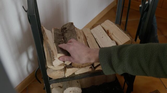 Hand placing split firewood logs into a metal stand for organized fuel storage in a home interior setting