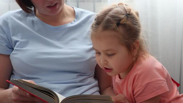 Close up of mother and a Caucasian little daughter are reading a book of fairy tales together. Concept of Mother's Day and preschool education.