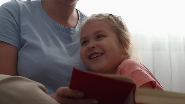 Close up of happy woman and smiling Caucasian little girl are reading book of fairy tales together. Concept of Mother's Day and preschool education.