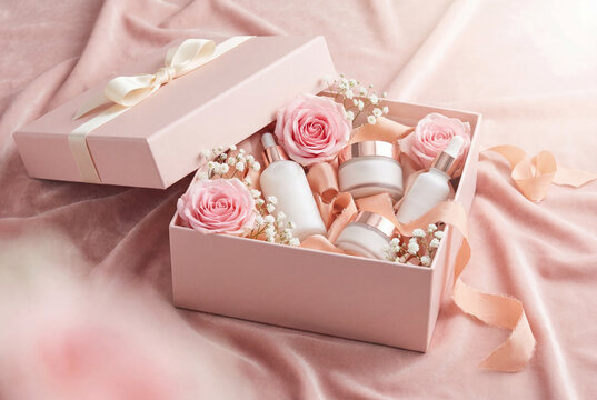 Pastel pink cosmetic gift set with beauty cream and serum bottles inside box with fresh roses