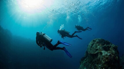 Obraz premium Three scuba divers exploring deep blue ocean with sunbeams and coral