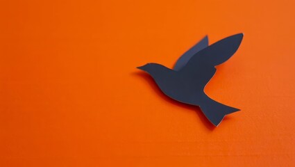 Obraz premium One paper black crow with raised wings in the upper right corner on an orange background with space for text.