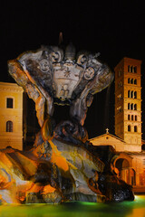 Beautiful baroque Fountain of the Tritons with medieval Basilica of Saint Mary in Cosmedin lit up at night in Rome