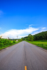 A road that cuts through rice fields and mountains, with green views and clear skies.