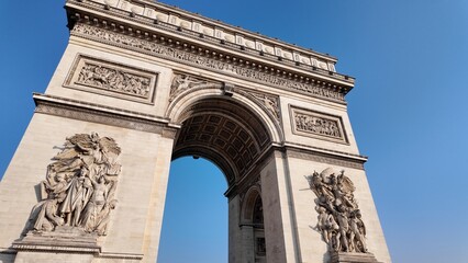 Obraz premium Arc de triomphe in paris, majestic triumphal arch with ornate stone carvings and reliefs, classical architecture against a bright blue sky, iconic national monument