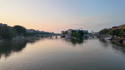 Seine river reflecting soft sunset colors with historic pont neuf arches and parisian buildings along tranquil urban banks at dusk, showing city life © DawDunia