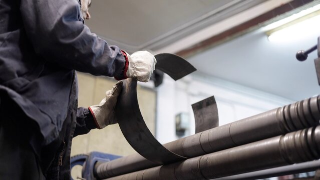 Skilled metal worker shaping metal sheet using industrial rolling machine for fabrication. Demonstrating precision and expertise in workshop environment