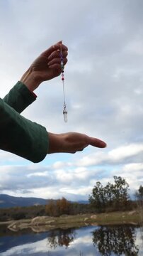 Person holding a quartz crystal pendulum for dowsing
