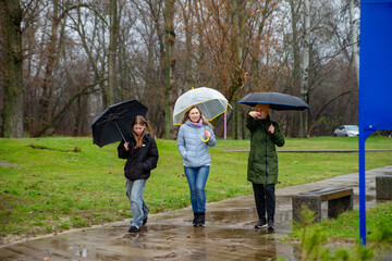 Three Generations of Women Walking Together in a Park on a Rainy Day Holding Umbrellas