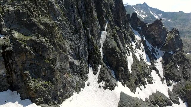 Aerial timelapse of sharp rocky alpine mountain peaks in summer across high altitude USA ranges. Rugged cliffs and exposed ridgelines reveal dramatic geology under clear blue sky.