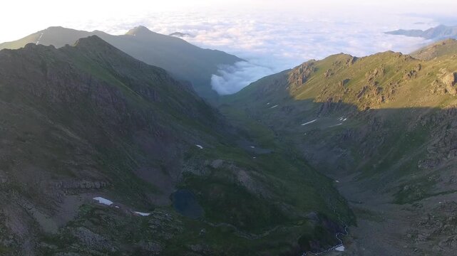Aerial view of alpine lake surrounded by tundra meadows in the Rocky Mountains at high altitude. Clear summer light reveals rugged peaks and pristine wilderness across remote American ranges.