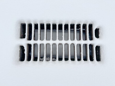 Cast iron drainage grate covered with snow during snowfall