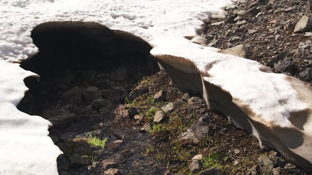 The stream formed by the melting snow waters on the mountain flows through the ice tunnel as it flows towards the alpine lake