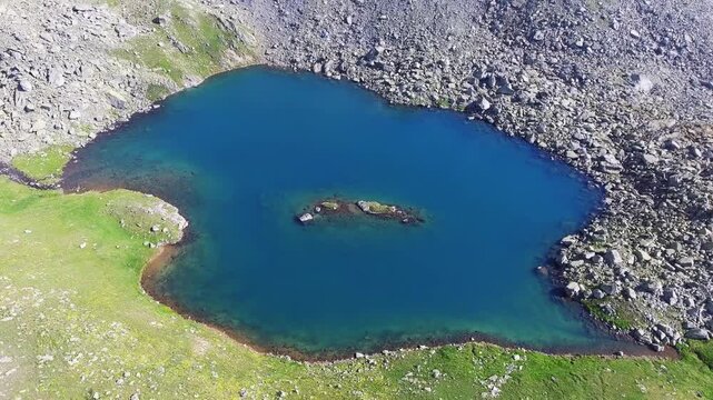 Aerial view of alpine lake surrounded by tundra meadows in the Rocky Mountains at high altitude. Clear summer light reveals rugged peaks and pristine wilderness across remote American ranges.