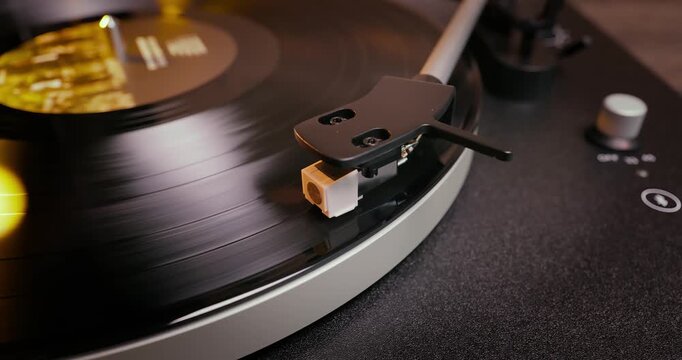 Detailed close-up of a turntable tonearm with white cartridge headshell, positioned over a black vinyl record on the platter, highlighting audio equipment precision.