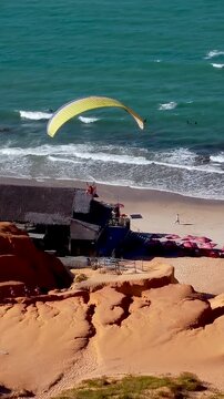 Parasailing Flying At Canoa Quebrada Ceara Brazil. Tourists Parasailing Over A Tropical Ocean On A Sunny Day. Shore Sky Clouds Beach Sea. Shore Beach Panorama. Canoa Quebrada Ceara.