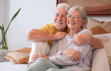 Portrait of happy handsome senior gray haired couple sitting together in bed looking at tv