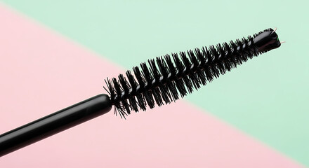Naklejka premium mascara brush close-up showing black bristles on a pastel pink and mint green background ideal for cosmetic product marketing.