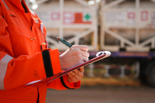 A safety officer is checking on safety checklist to verify the risk of chemical transportation with Liquid nitrogen tank on background. Industrial working scene, close-up and selective focus.
