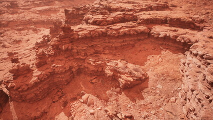 Vast red rock formations stretch across the arid desert under a clear sky. Erosion has created intricate layers and textures in the rocky terrain, inviting exploration and adventure.