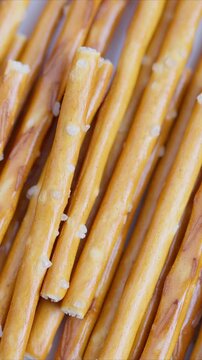 Closeup salted pretzel sticks arranged in tight rows showing golden baked texture and scattered salt crystals, studiolit minimal background, food still life, crisp crunchy snack