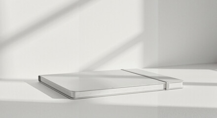 Naklejka premium Minimalist notebook placed on white tabletop with shadow patterns 