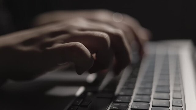 Close-up of hands typing on a laptop keyboard in low light conditions