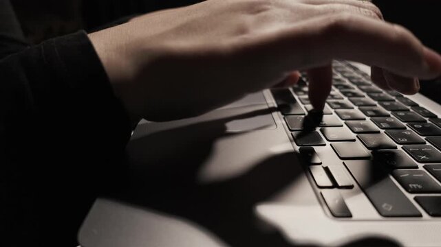 Close-up of hands typing on a laptop keyboard in low light conditions