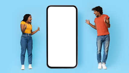 Emotional african american millennials stylish man and woman looking at big smartphone with white...