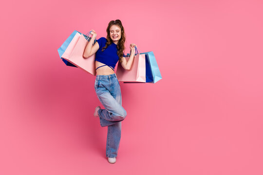Cheerful stylish young woman showcasing shopping haul in a trendy vibrant outfit against a bright pink backdrop