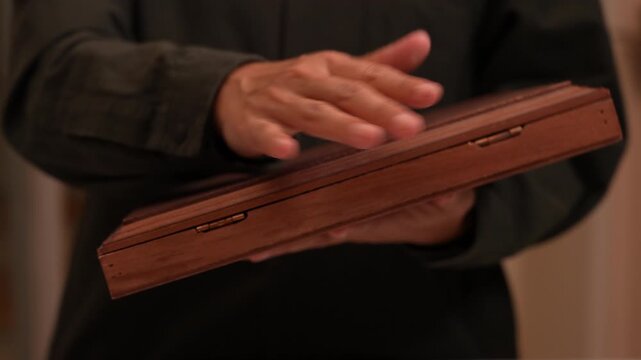 Close-up of hand dusting an old vintage wooden box, cleaning dust off antique wood surface, discovering hidden treasure and domestic maintenance concept.