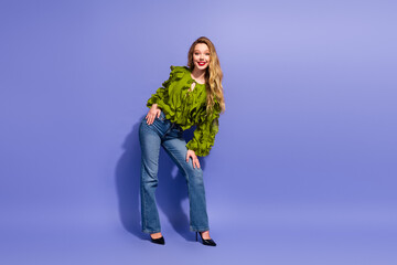 Charming young female model posing in lime green blouse and denim jeans against violet background...