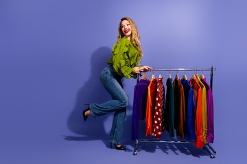 Charming young woman with colorful clothing rack smiles against purple background fashion and...