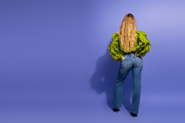 Charming young woman with blonde hair wearing bright green puff sleeves standing against purple...