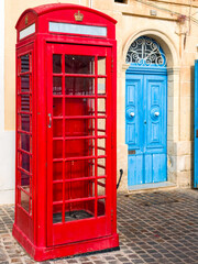 Marsaxlokk, Malta &ndash; Classic British-style phone booth as colorful accent in front of typical Maltese building with blue wooden door