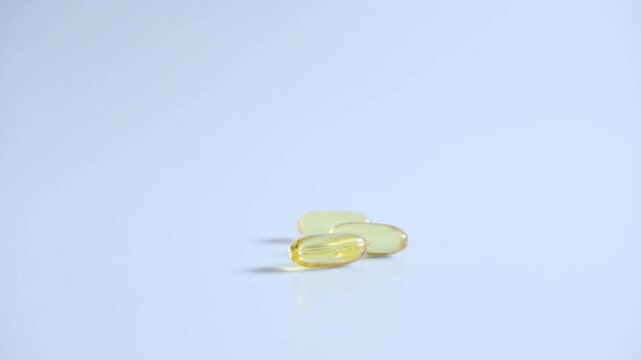 Fish oil capsules fell onto the white floor. Yellow capsules. Slow motion video.
