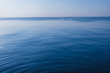 Fototapeta premium Calm Deep Blue Ocean Surface with Soft Ripples under Clear Sky,A serene and minimalist view of a vast, calm blue sea with gentle ripples on the water surface stretching to the horizon under a clear,