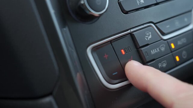 Finger pressing button on modern car dashboard with red indicator lights. Driver activating heated seat in modern car interior. Concept of temperature adjustment and driving comfort in cold weather
