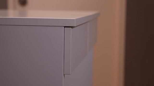 Close up of a person's hand slowly opening and closing a white wooden drawer of a minimalist desk in a bright, clean room.