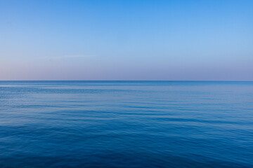 Obraz premium Calm Deep Blue Ocean Surface with Soft Ripples under Clear Sky,A serene and minimalist view of a vast, calm blue sea with gentle ripples on the water surface stretching to the horizon under a clear,