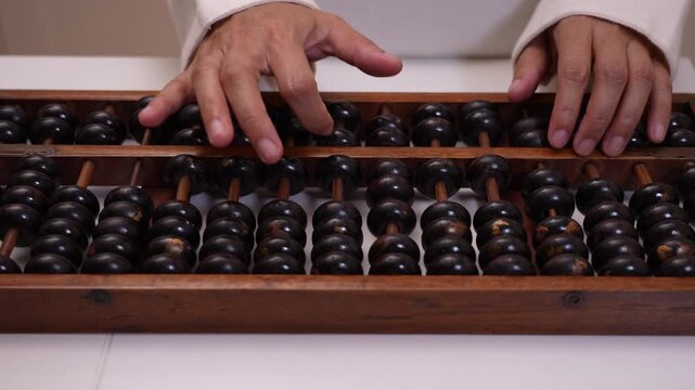 Close-up of hand using vintage abacus on white table for calculation, person counting and moving beads on traditional tool, business finance and mathematics education concept.