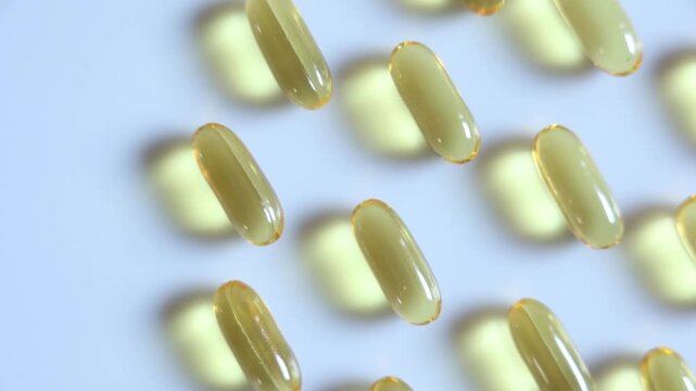 Close up Yellow fish oil capsules on the white floor. Slow motion video.