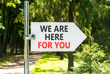 Support, help and we are here for you symbol. Concept words We are here for you on beautiful white road sign. Beautiful green garden background. Business we are here for you concept. Copy space.