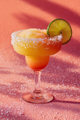 Frozen margarita cocktail with peach and citrus gradient, salt rim glass and lime garnish