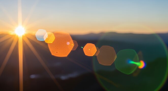 Sunset landscape with lens flares and bokeh effects over mountains and hills at dusk from a high viewpoint