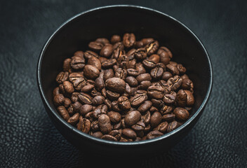Fototapeta premium Bowl of roasted coffee beans on dark surface