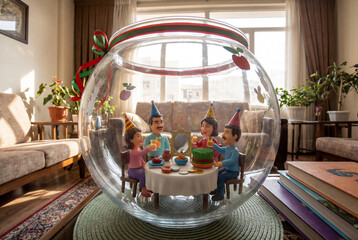 Miniature family figures celebrate a Nowruz inside a glass terrarium bowl on a coffee table in a sunny living room