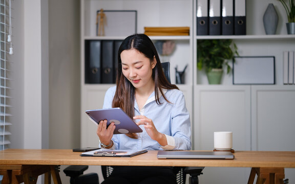 Businesswoman using a digital tablet to review financial data while sitting at her desk in a modern, well-organized office.