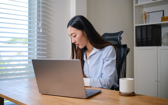 Professional businesswoman reviewing financial reports while working on a laptop at her desk in a bright modern office.